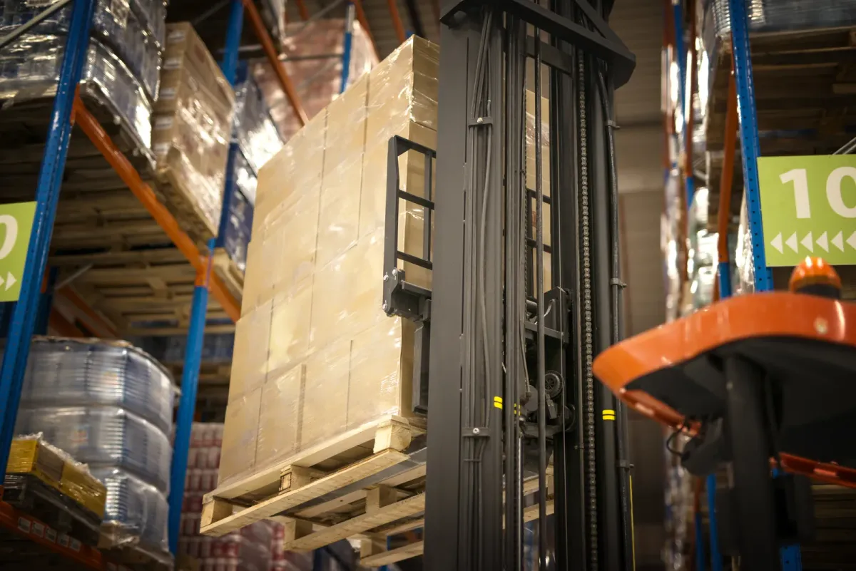 Palette de caisses en carton filmée, soulevée par un chariot élévateur dans un entrepôt : emballage tertiaire