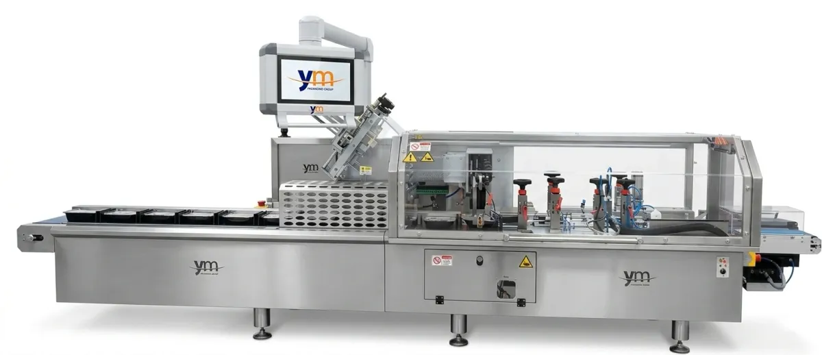 Machine de pose de fourreaux pour emballages rigides de YM Packaging, avec convoyeur de barquettes et pose de fourreaux en carton
