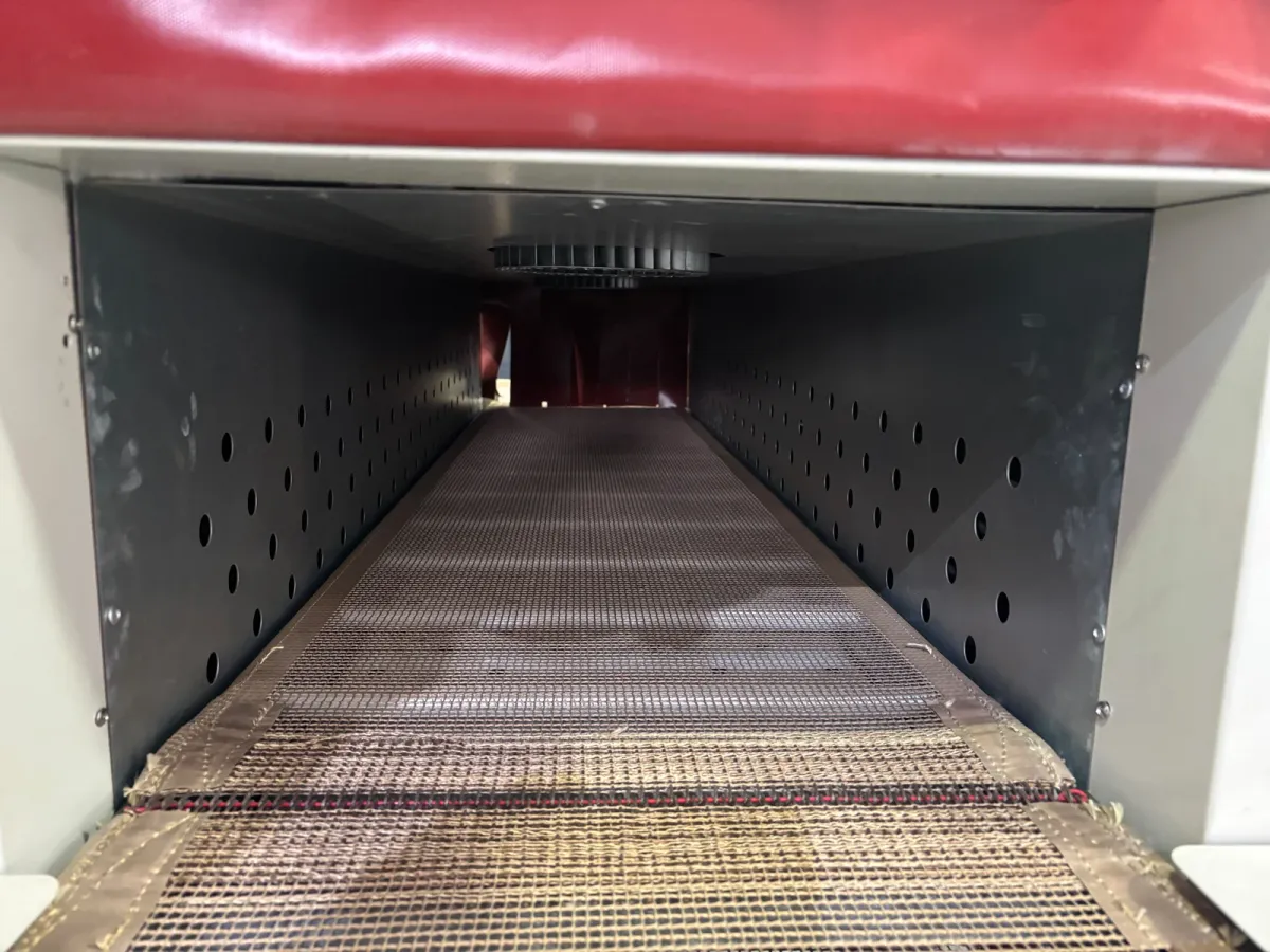 Inside the TR shrink tunnel: perforated hot-air walls and the mesh belt running to the outfeed