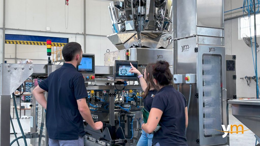 Een technicus en twee technici kijken naar het aanraakscherm van een horizontale verpakkingsmachine in een industrieel gebouw.